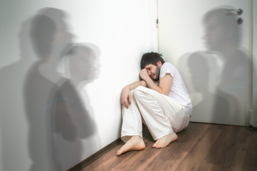 man crouching in fear in corner of room with shadows around him